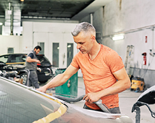 Mechanic in orange shirt works on a car